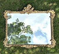 Full view of the antique gilt framed wall mirror showing detailed scroll and shell design in the frame and clear reflective glass with some wear.