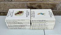 Stack of 21 Beatrix Potter hardcover books with white covers arranged in two neat stacks. Titles and illustrations visible on spine and front covers.