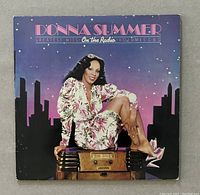 Front cover of the album featuring Donna Summer sitting on an antique radio with a cityscape background at night.