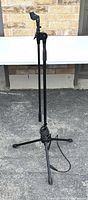 Front view of black Profile microphone tripod stand with boom arm, showing adjustable handle and attached cable coiled at base on ground.