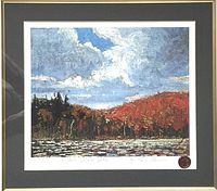 Framed print showing landscape with cloudy sky, red hillside and water body, signed and numbered edition visible.