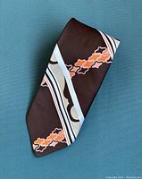 Folded view of the brown tie with diagonal white and light blue stripes and orange geometric accents.
