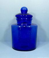 Front view of the cobalt blue glass jar with lid, showing cylindrical shape and rounded knob on lid.