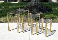 All three brass tone and smoke glass nesting tables arranged on sidewalk in sunlight showing full set and condition