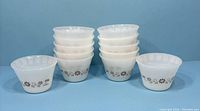 Stacked 12 vintage milk glass custard bowls with brown daisy floral pattern in a group.