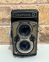 Front view of the camera showing Yashica-D label, two lenses, and control knobs.