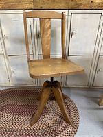 Full view of the wooden child's swivel chair showing seat, backrest, and base with legs on a braided rug.