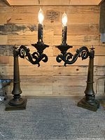 Front view of the pair of electrified antique swing arm candelabras on bronze pillar bases, lit to show working condition.
