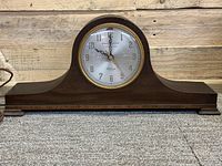 Front view of the wooden electric mantle clock showing the round clock face with brass bezel, Arabic numerals, and General Electric Telechron branding.