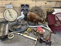 Overview of assorted barn finds including metal pig watering can, vintage scale, cast iron hooks, muffin pans, metal bread pan, bird figurine, metal fan-shaped red item, dried wheat bouquet, and small decorative pieces.