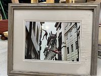 Framed photograph showing acrobats mid-jump between buildings with a matte and frame showing mildew/water damage