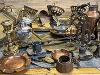 Overview of assorted copper, brass, and other metal antique and vintage items arranged on a surface showing tarnish, wear, and patina.