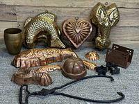 Photo showing vintage copper molds shaped like a fish, heart, lobster, crab, pumpkin, and shell, a brass cup, iron ice tongs, and star-shaped cutter unclear in use