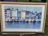 Front view of framed watercolor painting showing colorful harbor scene with boats and buildings. Tape measure and marker included for scale.