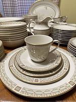 Photo of the full White Nile set showing stacked plates, bowls, a creamer, and cups on wooden surface.