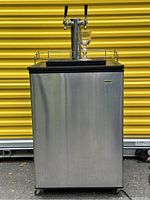 Front view of Haier kegerator with tap tower and glass on top against yellow background