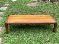 Full view of the rectangular wooden coffee table set on grass outdoors, showing top surface and legs.