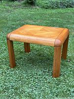 Side view of the rectangular solid oak Mid-Century Modern side table on grass, showing rounded edges and wood grain detail