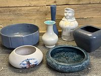 Seven mid-century art pottery items arranged on wooden floor, various styles and glazes visible