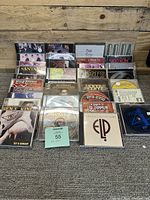 Photo showing the collection of 34 music CDs arranged on the floor against a wooden wall, featuring a variety of classic rock and blues artists in their open jewel cases.