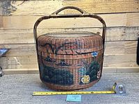 Front view of round woven bamboo basket with painted landscape and measuring tape for size reference