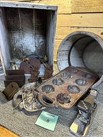 Old wooden crate with metal and cast iron items inside, showing various vintage kitchenware and primitives.