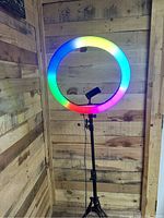 Multicolor RGB ring light illuminated showing color options, mounted on tripod with phone holder.
