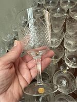 Hand holding a single vintage German crystal wine glass showcasing the intricate cross-hatch etched pattern and clear crystal with a stemmed base, with a sticker label on the base.