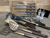 Cutting knife set in box with black-handled knives and various vintage kitchen utensils laid out on wooden surface