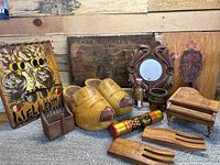 Photo showing an arrangement of vintage wooden decor items including a primitive 'Welcome' sign with owl design, Dutch clogs, carved mirror frame, small chair model, wooden holders, painted cylinder, bowl, and a vintage wooden advertisement sign.