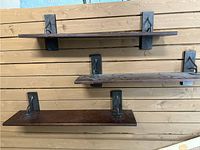 Three dark stained solid wood wall shelves mounted on a wooden wall with black iron brackets beneath each shelf.