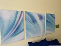 Three abstract painted canvases hung on a wall showcasing blue and lavender flowing patterns