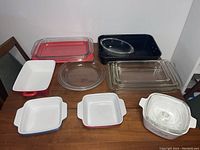 Top view of the assorted bakeware including clear Pyrex glass dishes, ceramic dishes in white and black, arranged on a wooden table.