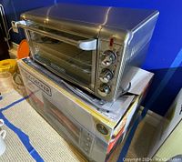 Black & Decker air fry convection oven on top of original box, stainless steel finish with three control knobs on the side.