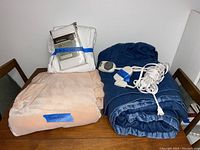 Image of blankets and electric blanket including wool blanket labeled GlenVen, navy blue electric blanket with controller, and white linen set.