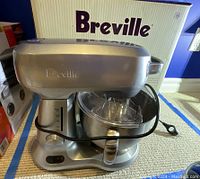 Silver Breville stand mixer assembled with bowl and splash guard in front of original Breville box