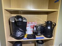Keurig coffee maker, toaster, coffee thermos, coffee mugs on shelf