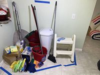 Wide view of lot showing step stool, mop bucket with wringer, waste bin, mops, brooms, vacuum cleaner, gloves, cleaning cloths and sponges arranged on floor marked as lot 178.