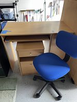 Desk with sliding keyboard tray and cabinet storage along with blue swivel chair positioned next to it.