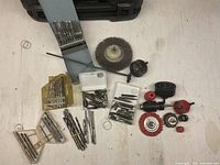 Multiple drill bits sorted in plastic holders and boxes alongside several wire brush and flap wheel attachments as well as hole saws and polishing wheels.