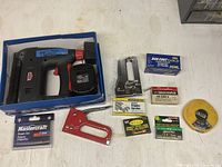 Electric staple tool, two hand staplers, and multiple boxes of staples spread on a flat surface.