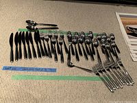 Photo of flatware pieces arranged in rows on carpet showing knives, forks, spoons, and serving utensils for 8 settings.