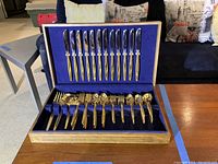 Full view of the open wooden case displaying the entire flatware set with gold electroplated handles and blue fabric lining.