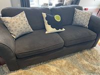 Front and angled views of the gray fabric sofa with three cushions and three decorative pillows in a living room setting.