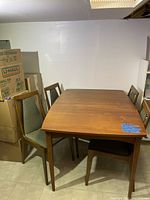 View of rectangular wood veneer mid-century modern dining table with four matching chairs in a basement setting.