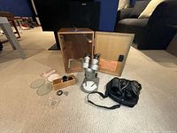 Microscope, accessories, and wooden case with binoculars on carpeted floor.