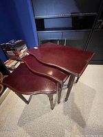 Three reddish-brown wooden nesting tables stacked together, showing their shape and leg style.