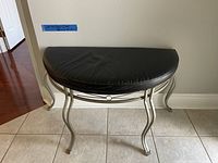 Full view of the oval bench showing silver metal frame and black upholstered seat