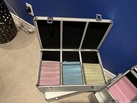 Open aluminum storage case showing internal compartments with three sets of colored sleeves in pink, blue, and yellow for discs.