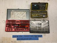 Photo showing three tool sets: a ratchet set in a red case, a mini screwdriver set in a black clear plastic case, and a socket set in a yellow metal case.